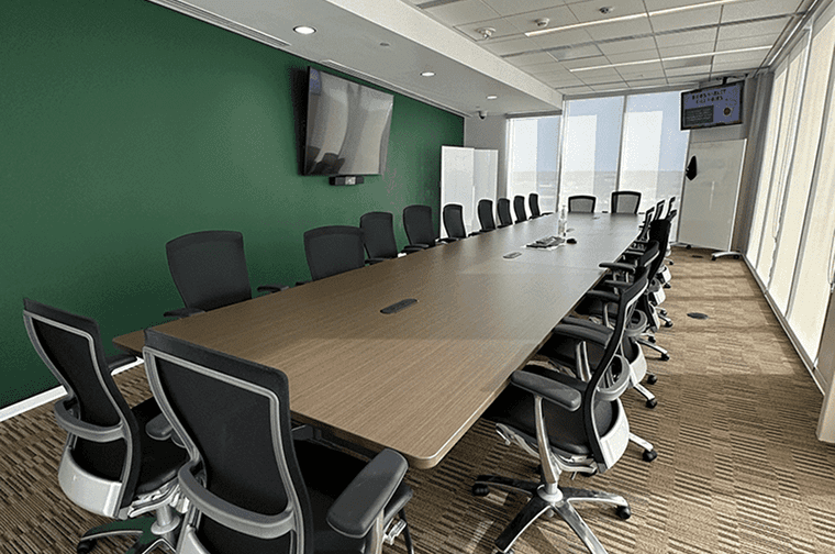 a large boardroom with a conference table surrounded by executive chairs, one wall is a deep green