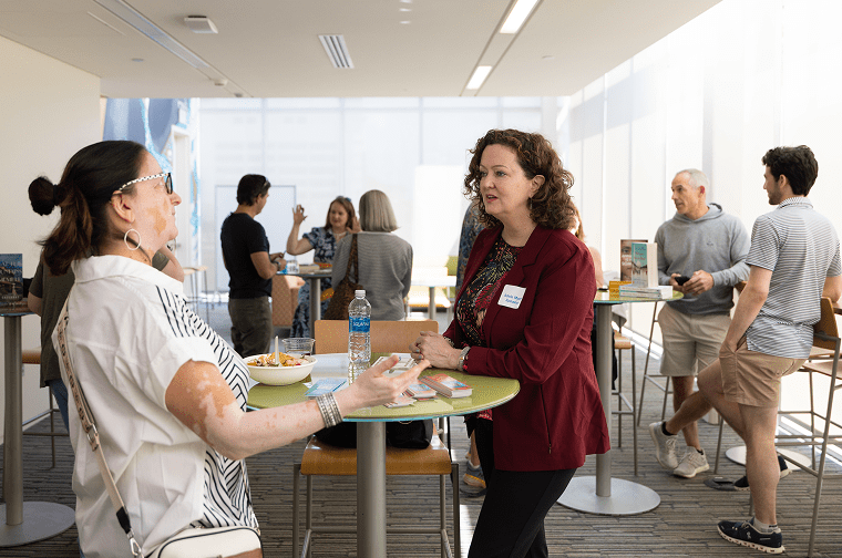 two ladies converse at a standing table while lively guests talk in the background
