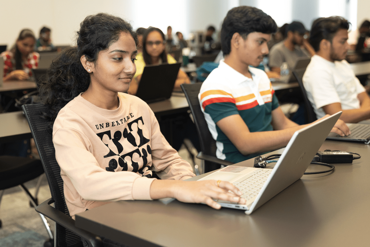 smiling students learning on laptops in a large classroom