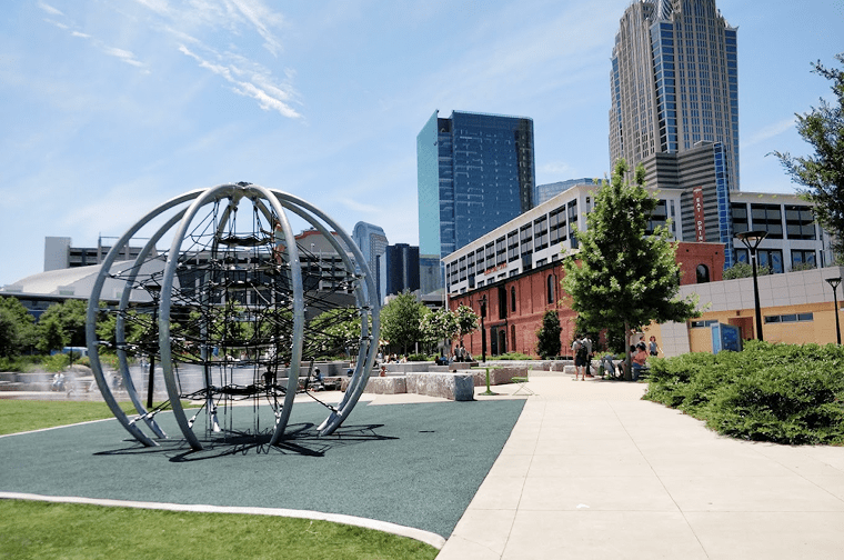 a globe sculpture in an urban park, tall buildings are seen in the distance
